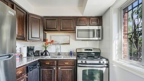 Una cocina con armarios de madera oscura, electrodomésticos de acero inoxidable, encimera de granito y ventana con vistas al verdor.