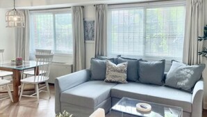 Una sala de estar moderna con un sofá gris, una mesa de centro de vidrio y un comedor con una mesa de madera y sillas blancas.