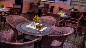 A restaurant with wicker furniture, round tables, and potted plants. - Remo Majestic Hotel (Sagamu)