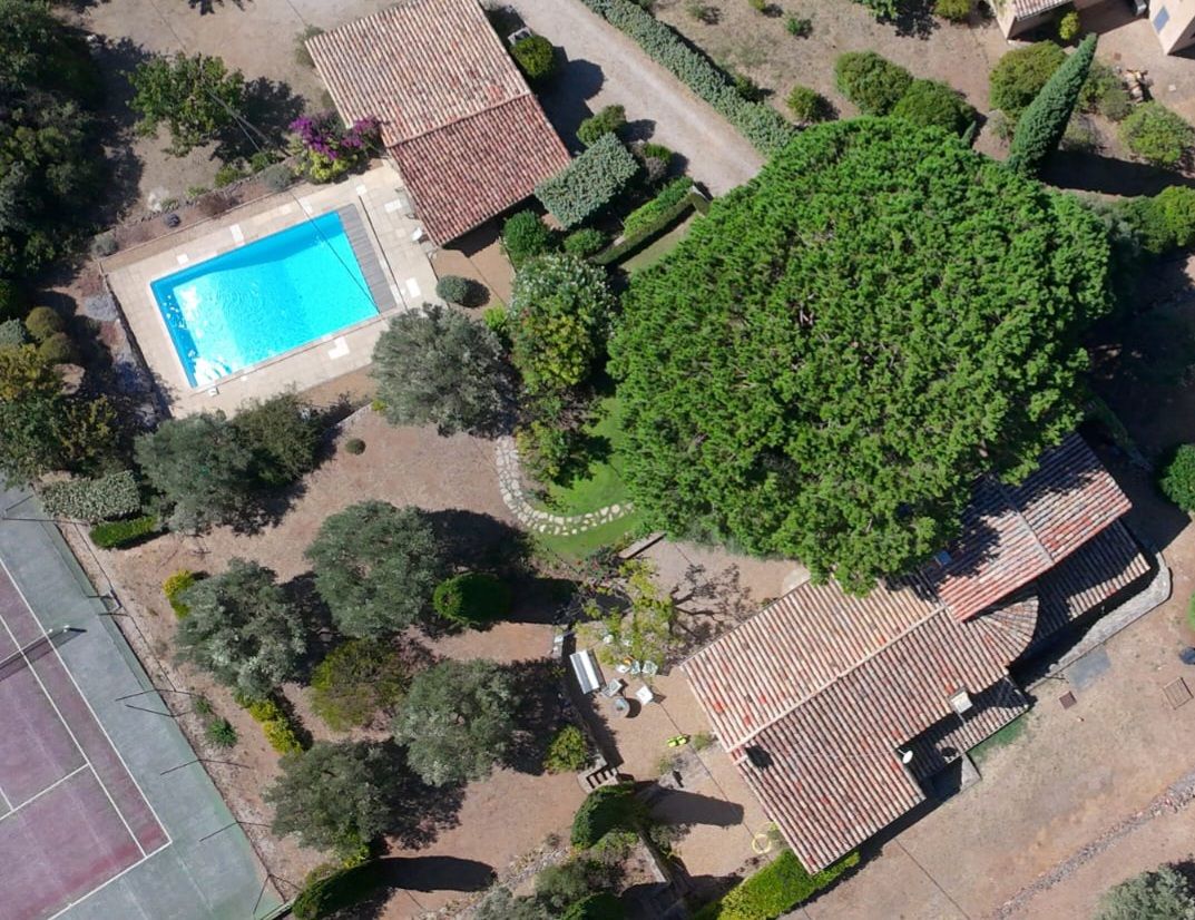 An aerial view of a residential property with a swimming pool, a tennis court, and a large tree.