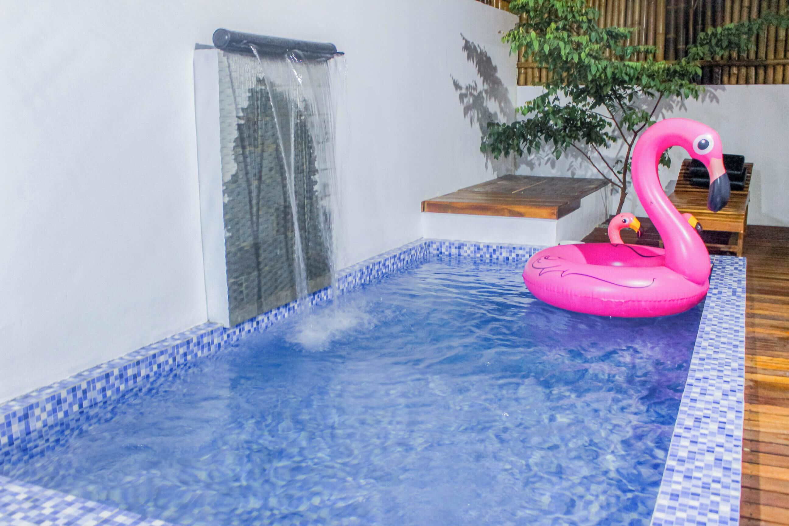 A hot tub with a pink flamingo float, a waterfall feature, and a wooden deck area.