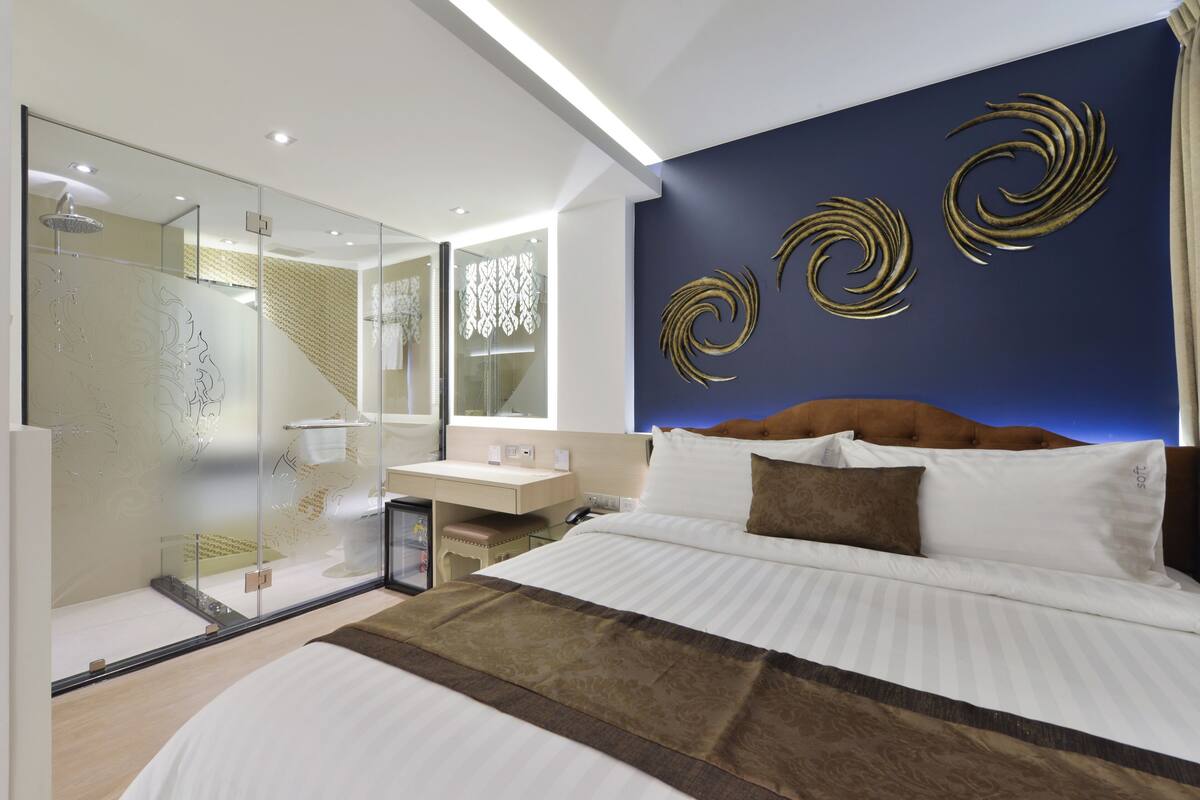 Una habitación de hotel moderna con una cama grande, una ducha con cerramiento de vidrio, un tocador con espejo y arte decorativo en la pared.