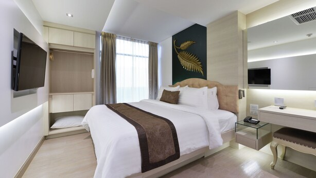 Une chambre d’hôtel moderne dotée d’un grand lit, d’un bureau avec un plateau en verre, d’un téléviseur à écran plat fixé au mur et d’une grande fenêtre avec des rideaux.