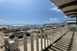 Egy tengerparti kilátás, fehér kerítéssel, strandhálókkal, napernyőkkel és tiszta, kék éggel.