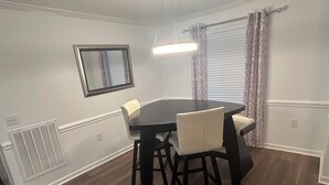 A dining room with a round table, four chairs, a ceiling light, a window with curtains, and a vent on the wall. - Luxury Apartment In Charlotte  (Charlotte)