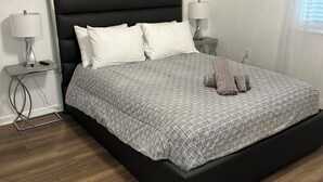 A modern bedroom with a black headboard, a patterned bedspread, two bedside lamps, and a wooden floor. - Luxury Apartment In Charlotte  (Charlotte)