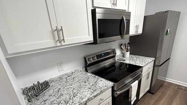 A modern kitchen with white cabinets, a stainless steel microwave, a black stove, and a refrigerator. - Luxury Apartment In Charlotte  (Charlotte)