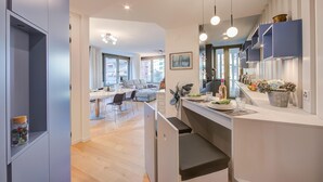 Een moderne keuken met een centraal eiland, hangende verlichting en uitzicht op de eethoek.