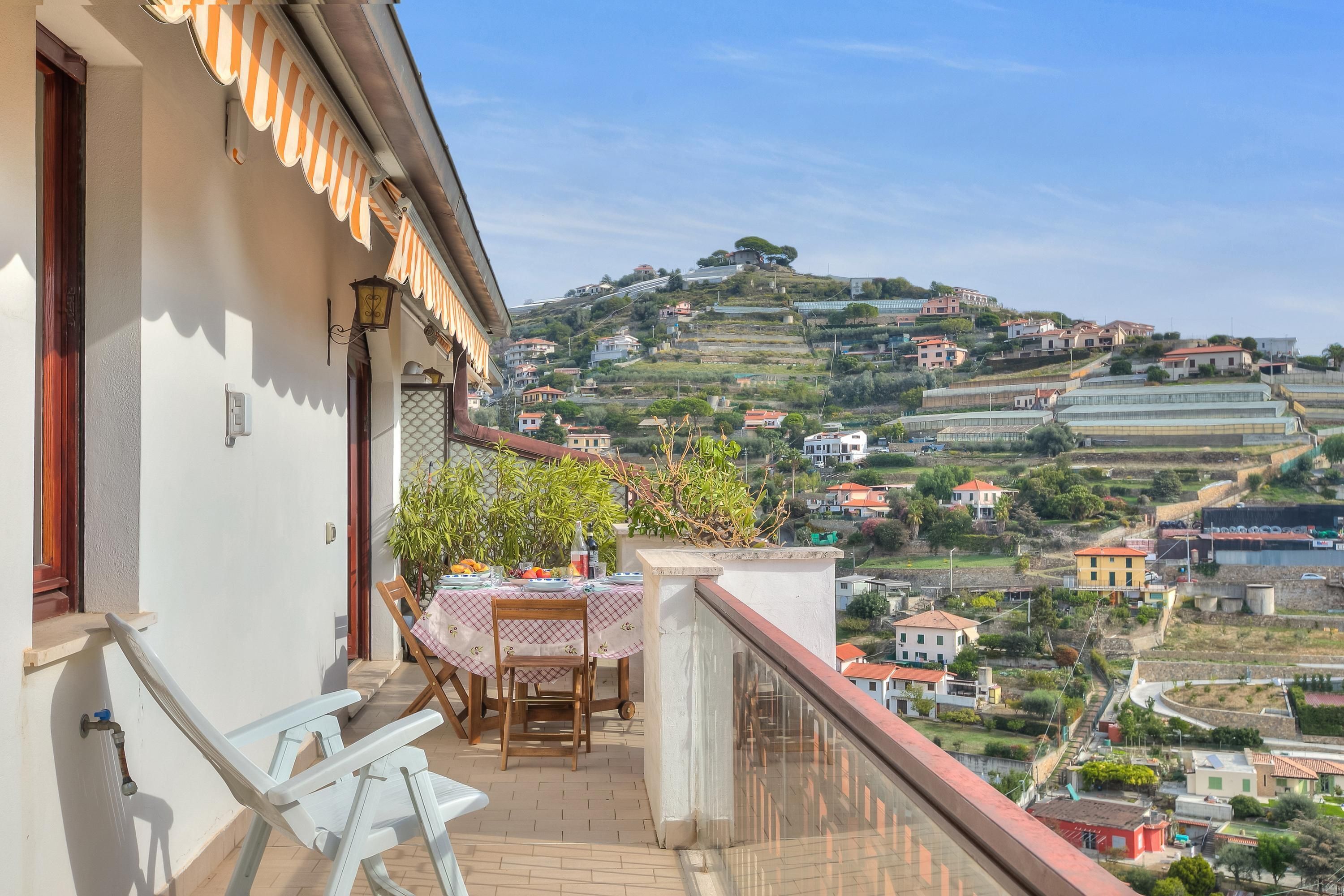 A balcony with a table set for dining, overlooking a hillside with houses.