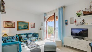 A modern living room with a sofa, coffee table, and TV. There are paintings on the wall and a balcony with a view. - Rhapsody By The Sea in Sanremo (Sanremo)