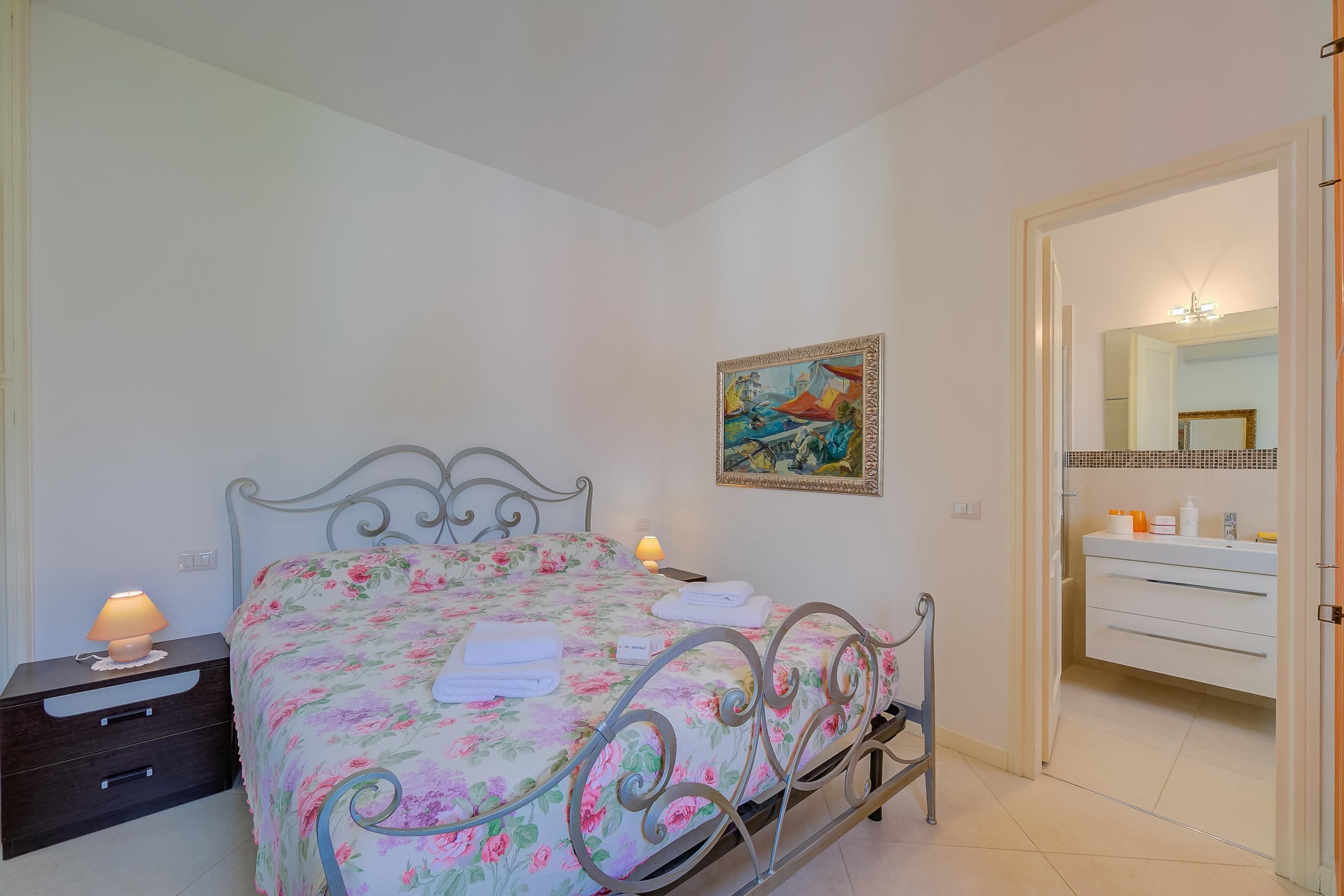 A bedroom with a bed, nightstand, and a painting on the wall.