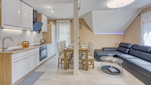 A modern kitchen with white cabinets, a wooden countertop, and a dining area with a table set for four. - Urban Oasis With Terrace And Parking (Zagreb)