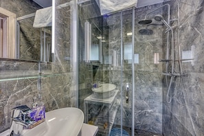 A modern bathroom with a glass-enclosed shower, a white sink, and a marble-tiled wall.