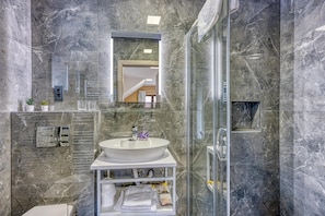 A modern bathroom with a marble wall, a glass-enclosed shower, a white sink, and a mirror.