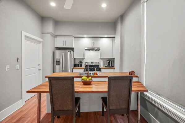 A compact kitchen with white cabinets, a wooden dining table, and two chairs.