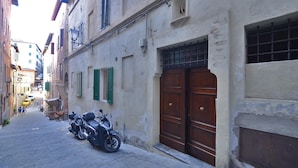 Una calle estrecha con motocicletas estacionadas y un edificio con puerta de madera y contraventanas verdes.