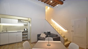 Una cocina moderna con armarios blancos, una mesa de comedor con sillas, un sofá y una escalera con barandilla iluminada.