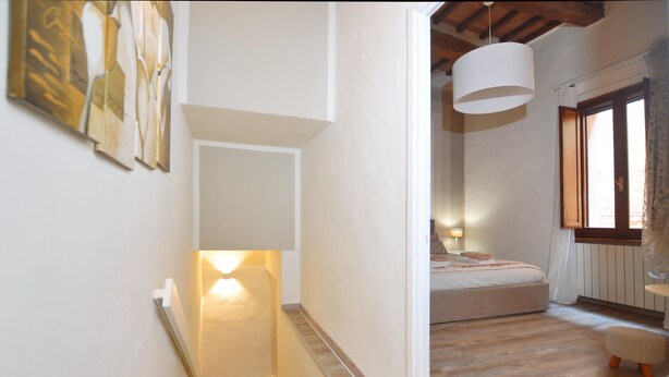 Un dormitorio con cama, mesita de noche, lámpara colgante y ventana con cortinas.