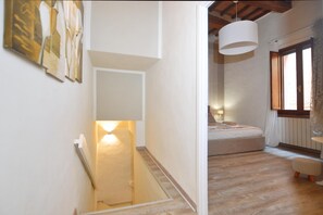 A bedroom with a bed, a bedside table, a hanging light fixture, and a window with curtains. - Casina Di Giada in Siena (Siena)
