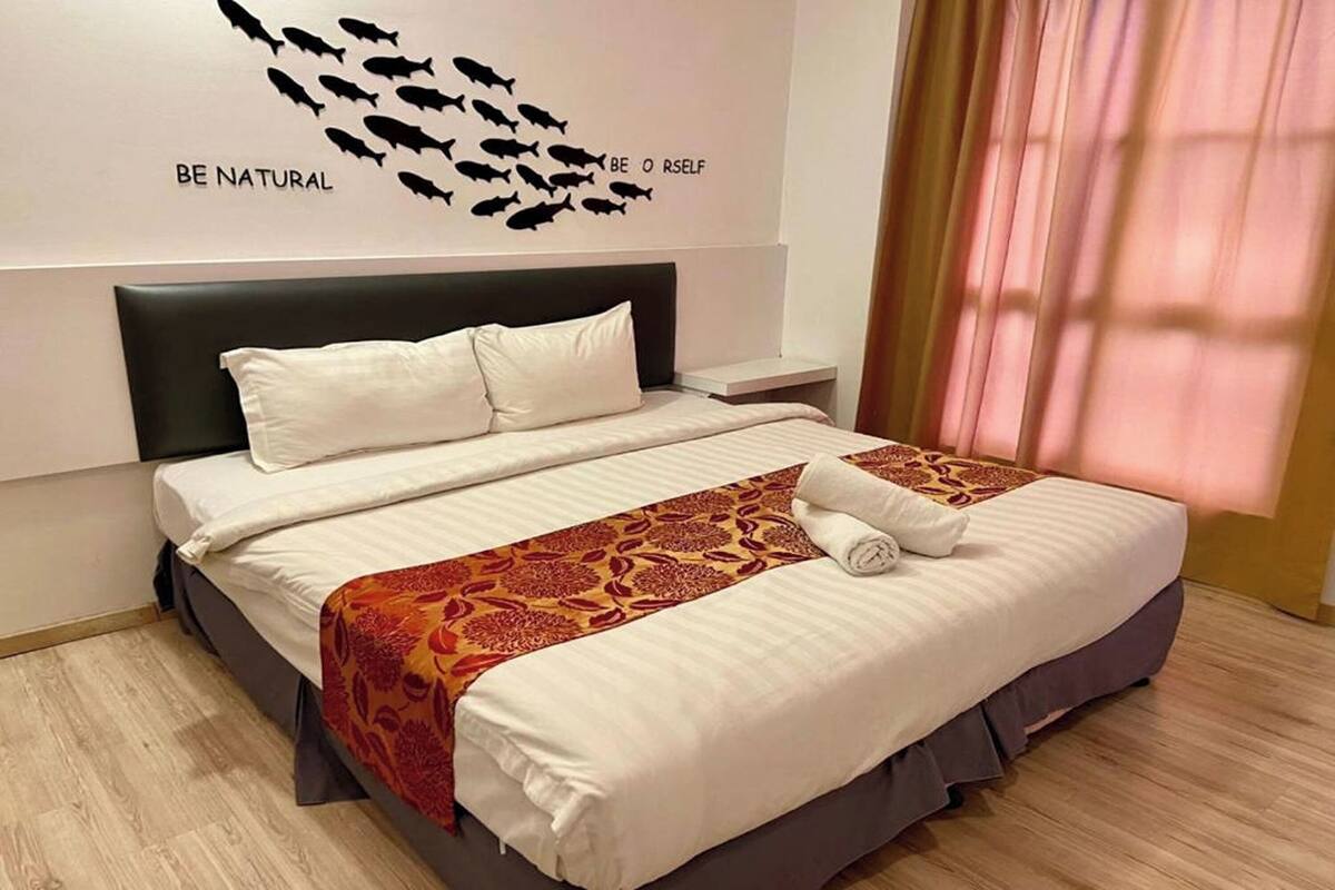 A hotel room with a bed, a nightstand, a wall decoration, and a window with curtains.