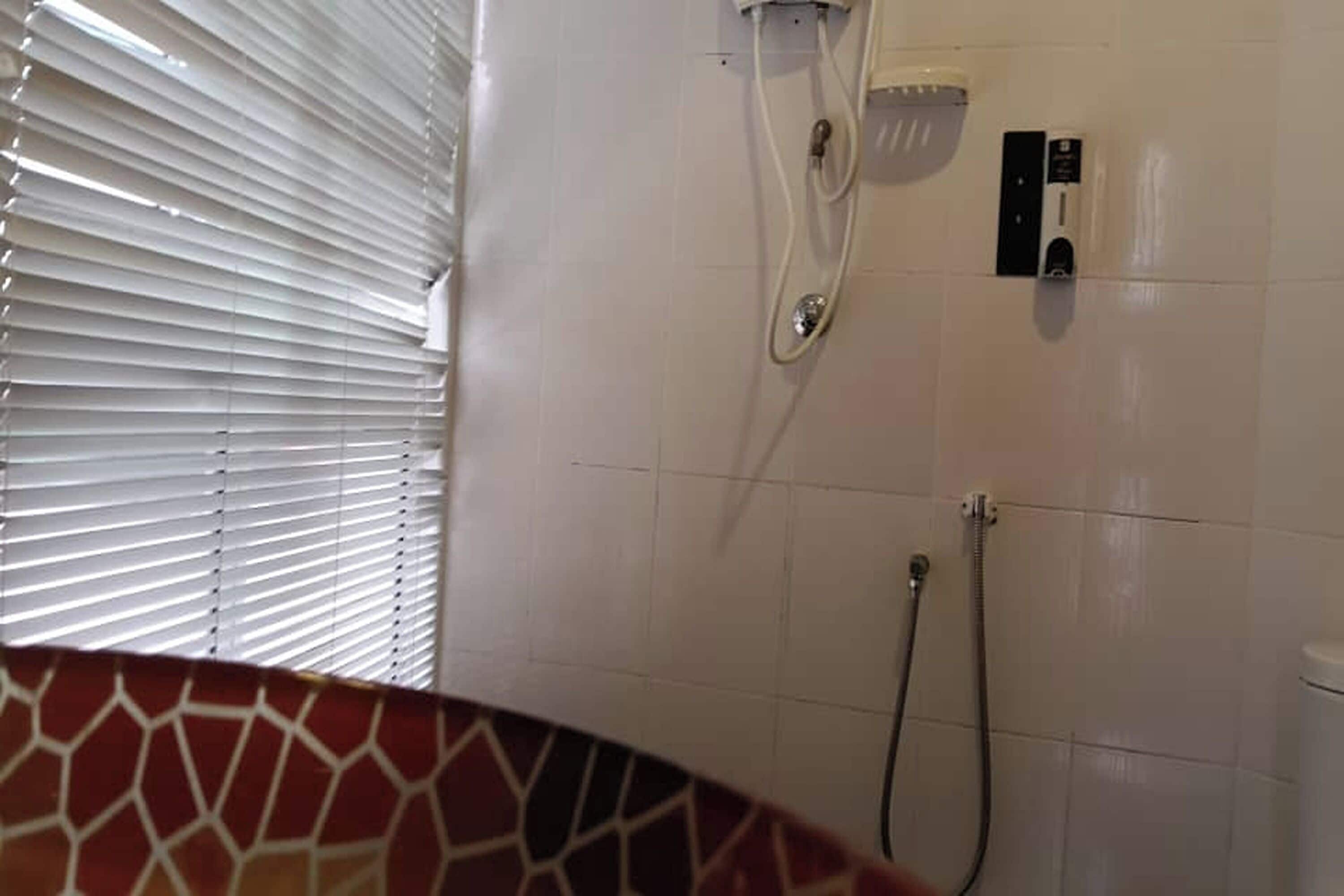A bathroom with a shower, a toilet, and a window with blinds.
