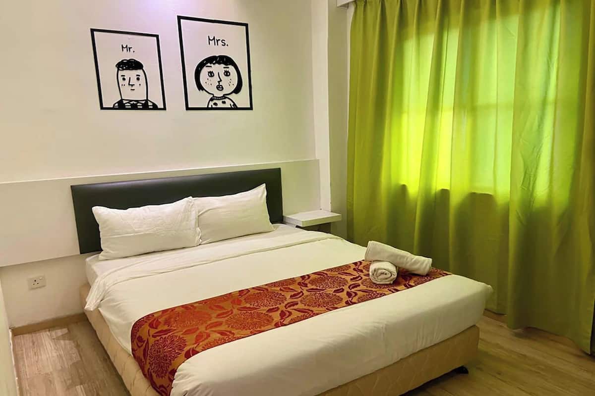 A hotel room with a bed, white bedding, a patterned throw, a nightstand, and a green curtain.
