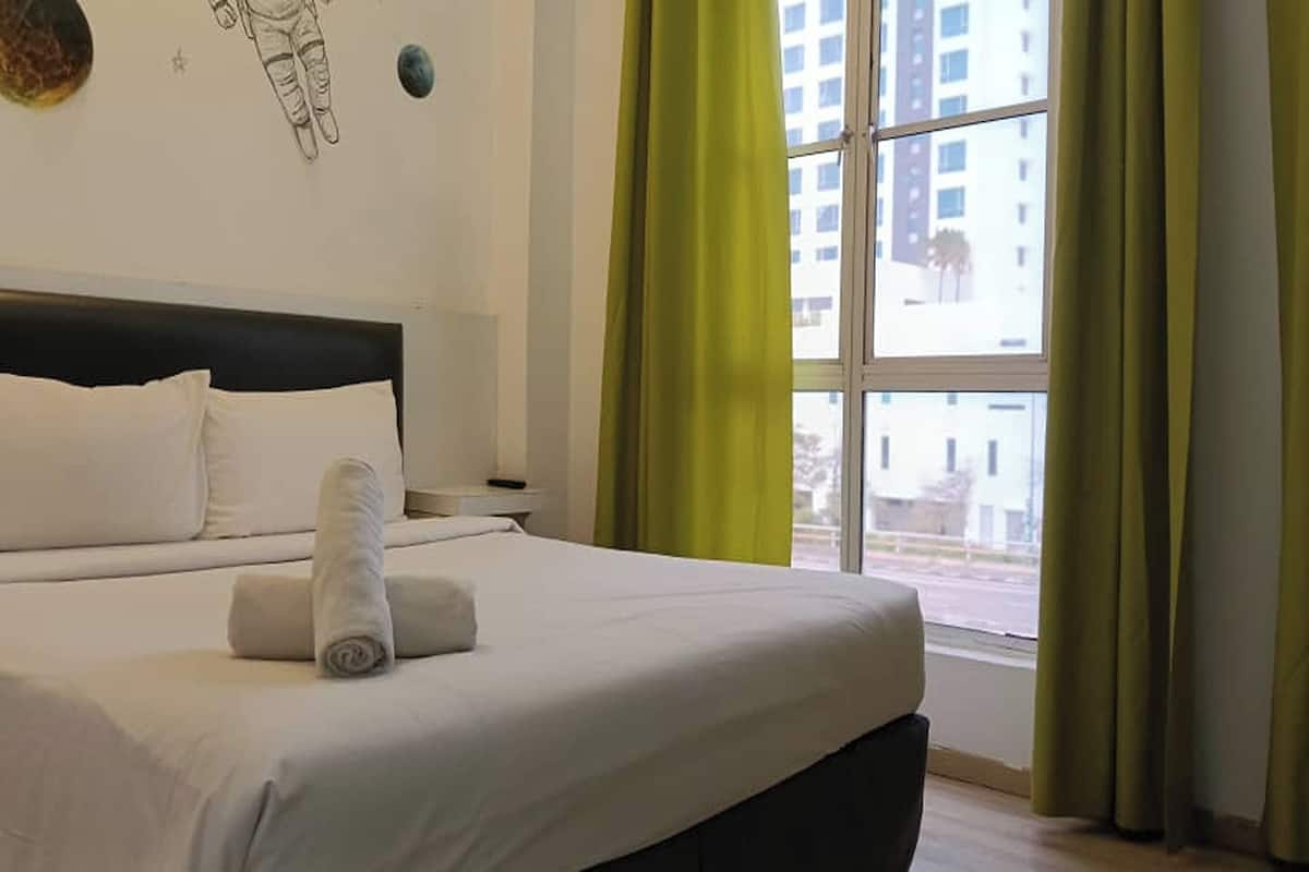 A hotel room with a bed, a nightstand, a window with curtains, and a wall decoration.