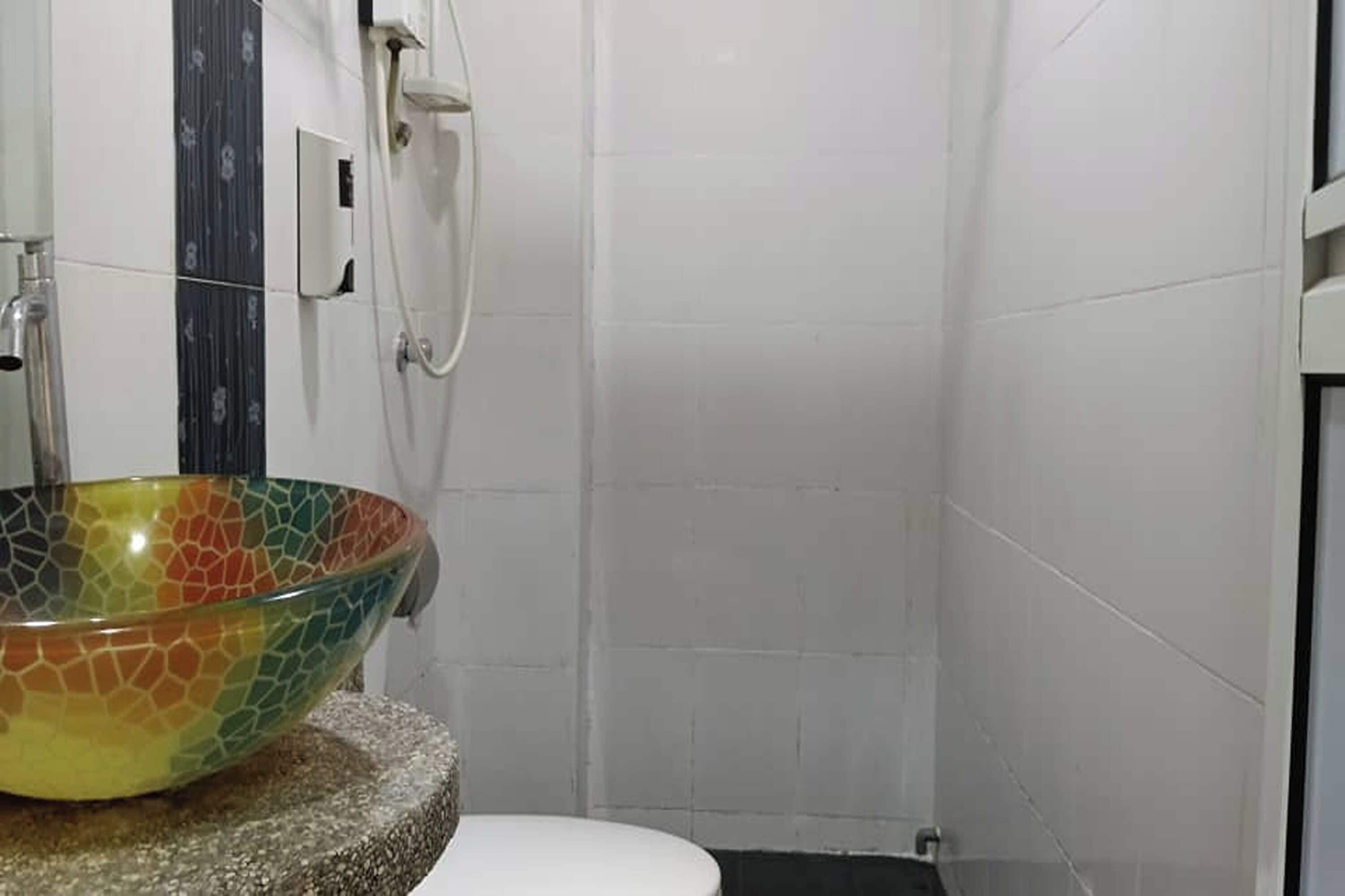 Een badkamer met een wastafel van mozaïek, een wit toilet en betegelde muren.