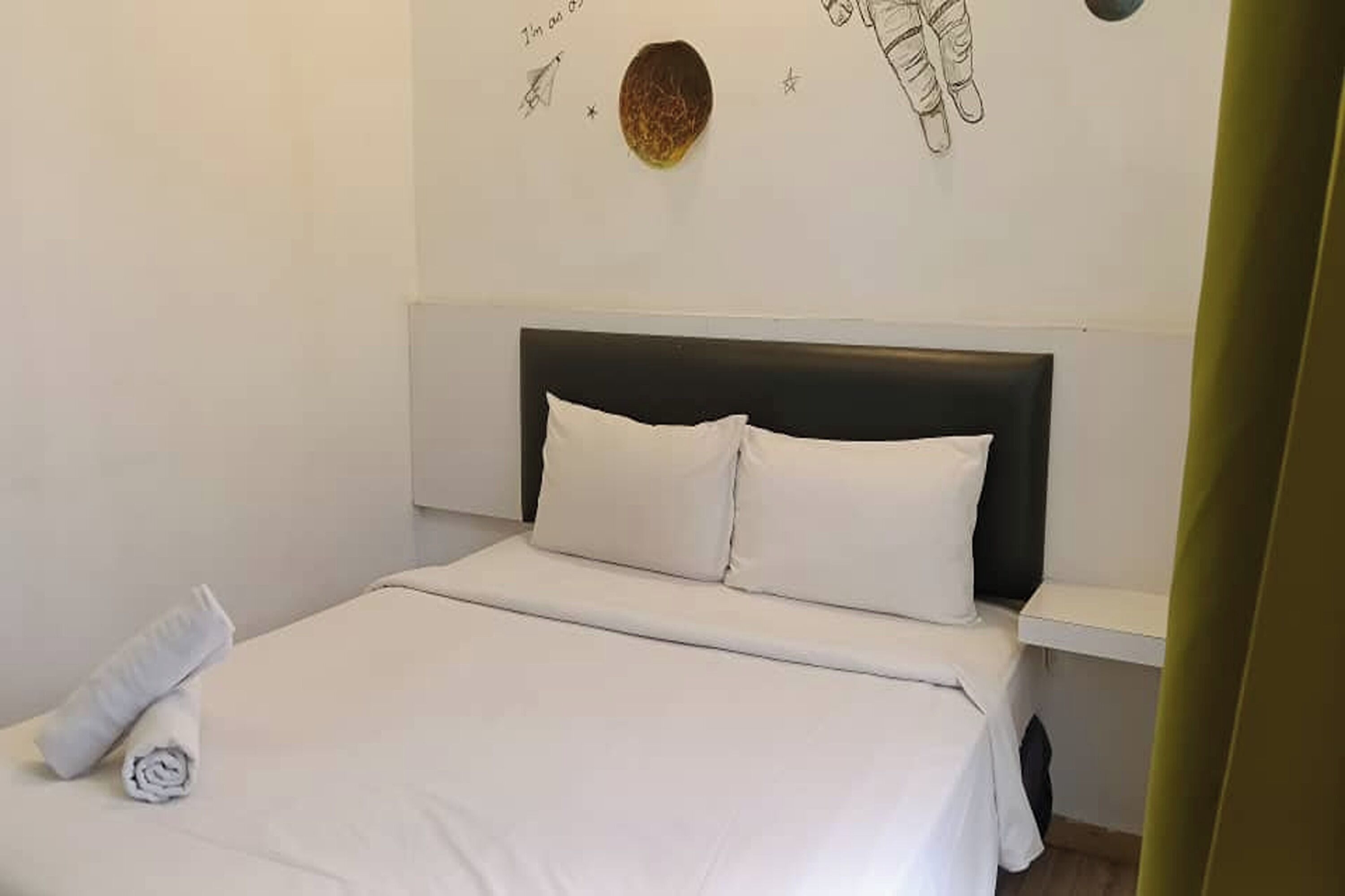 Una cama bien hecha con sábanas y almohadas blancas, una mesita de noche y un adorno en la pared.
