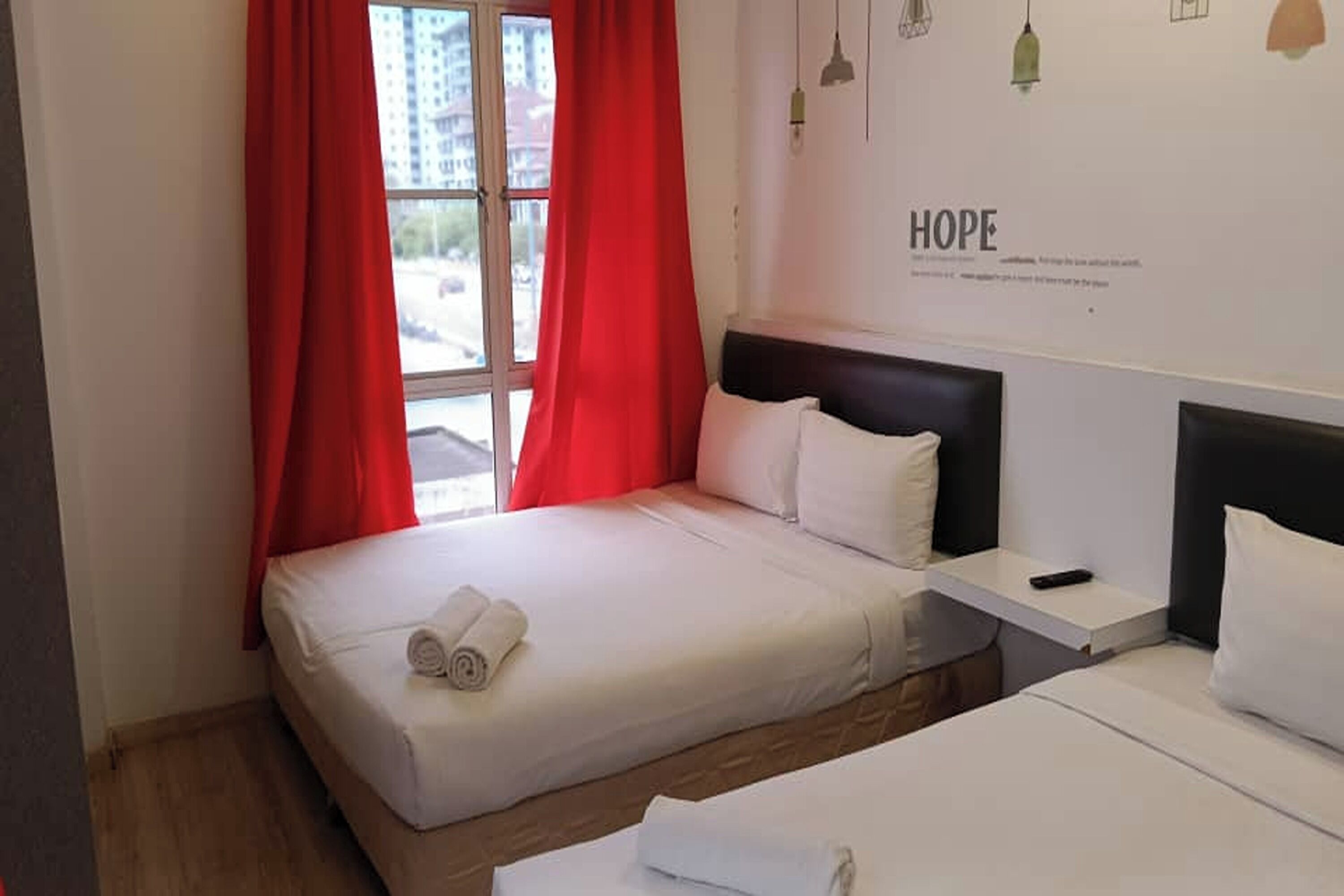 Een hotelkamer met een bed, nachtkastje en een raam met rode gordijnen.