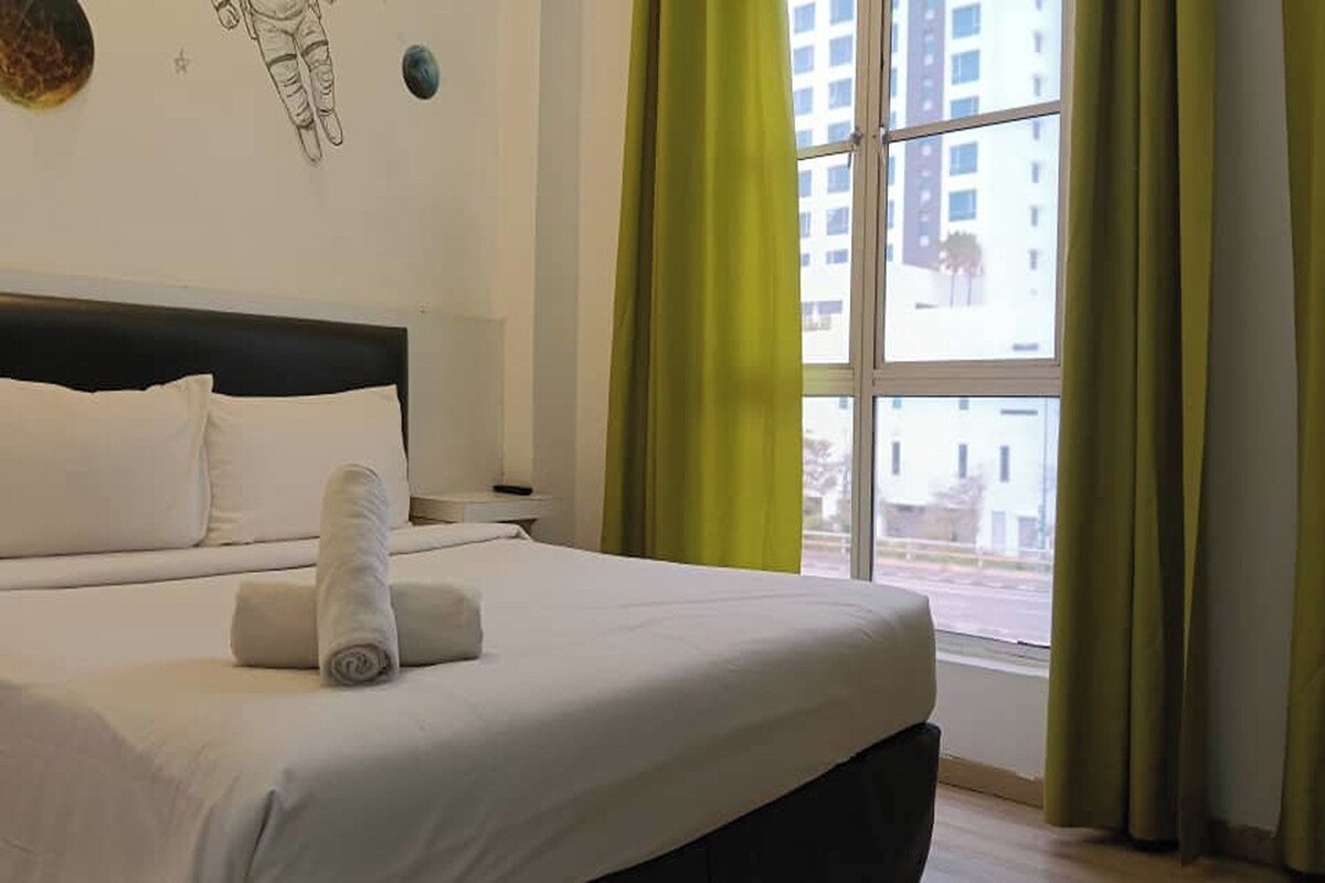 A hotel room with a bed, a nightstand, a window with curtains, and a wall decoration.