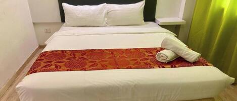 A neatly made bed with white linens, a red patterned bedspread, and a rolled towel on the side.