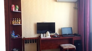 Hotellihuone, jossa on työpöytä, televisio, kannettava tietokone, pieni jakkara, hylly, jossa on pientä purtavaa, ja patteri.
