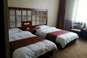 Habitación de hotel con dos camas, cabecera, mesita de noche, una silla y vistas al exterior.