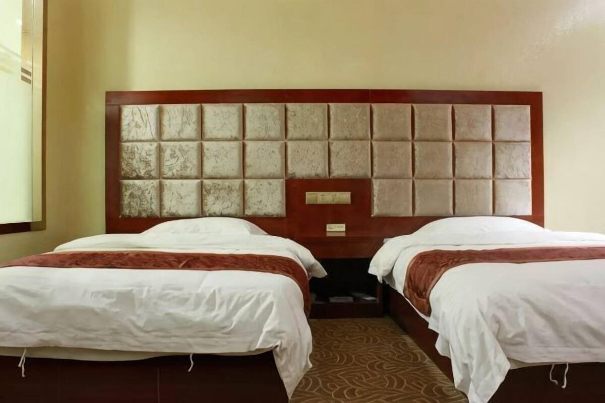 A hotel room with two beds, a wooden headboard, and a patterned carpet.