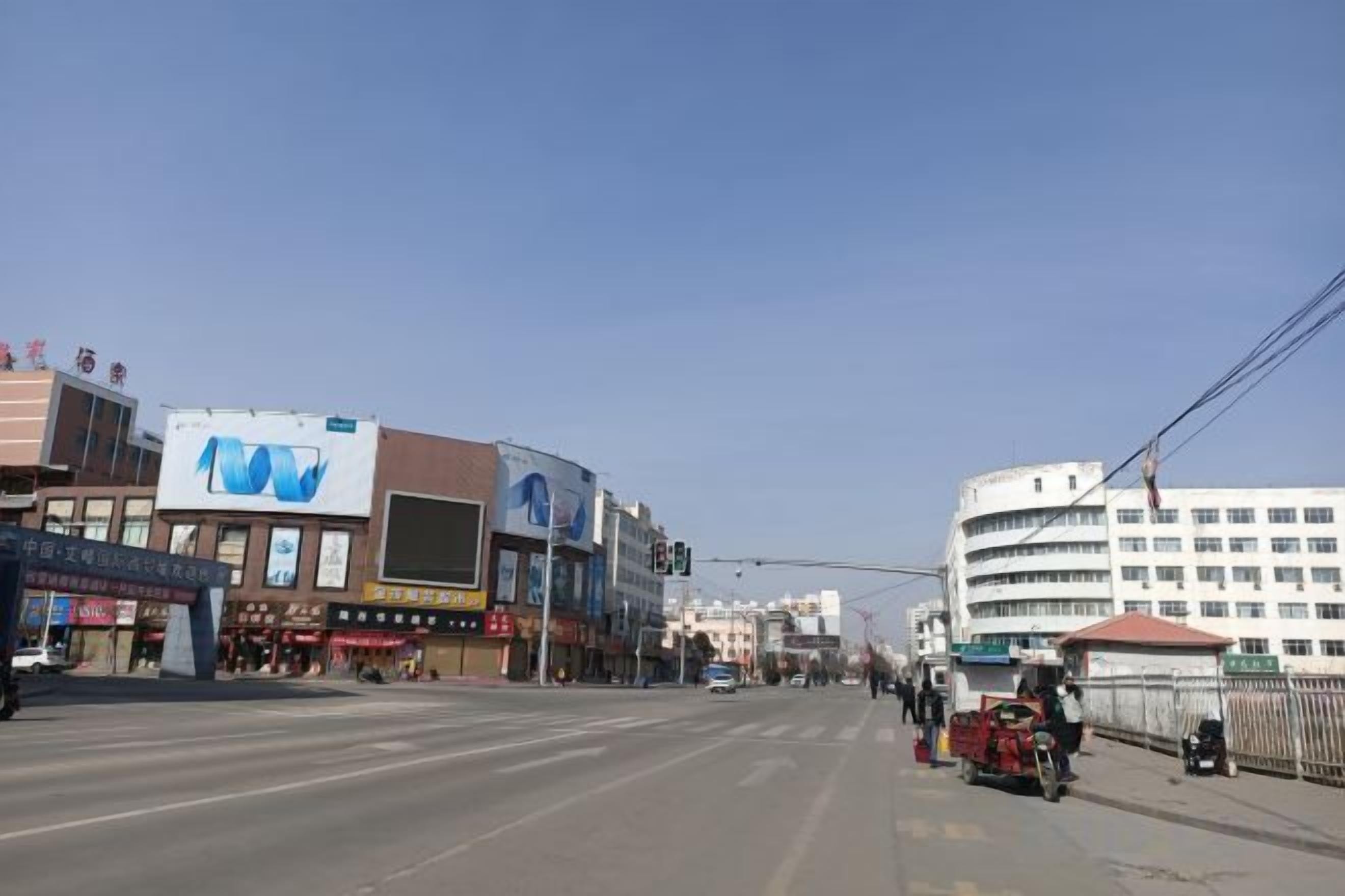 A street view with buildings, a clear sky, and a few vehicles.