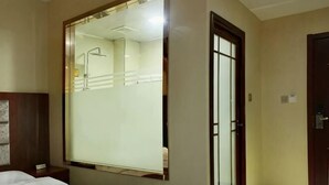 Hotellihuone, jossa on suuri peili, sänky, puinen pääty, ovi ja pieni yöpöytä.