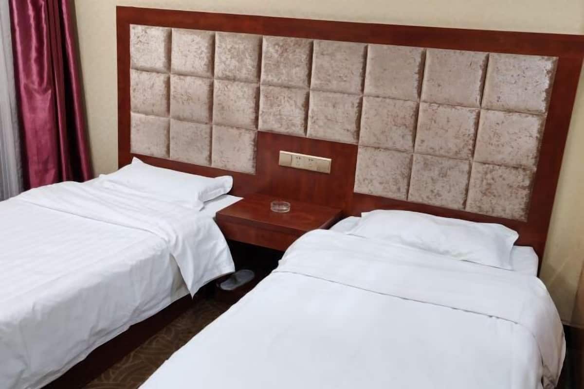A hotel room with two single beds, a wooden headboard, a nightstand, and a red curtain.