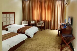 Habitación de hotel con dos camas, un escritorio, una silla, un televisor y una ventana con cortinas.