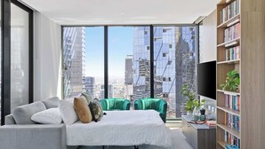 Un dormitorio moderno con un ventanal grande, una cama, un sofá verde, una estantería y un escritorio con una planta.
