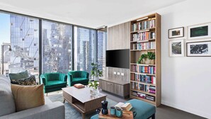 Ein modernes Wohnzimmer mit einem großen Fenster, grünen Sesseln, einem Couchtisch und einem Bücherregal.