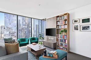 A modern living room with a large window, green armchairs, a coffee table, and a bookshelf.
