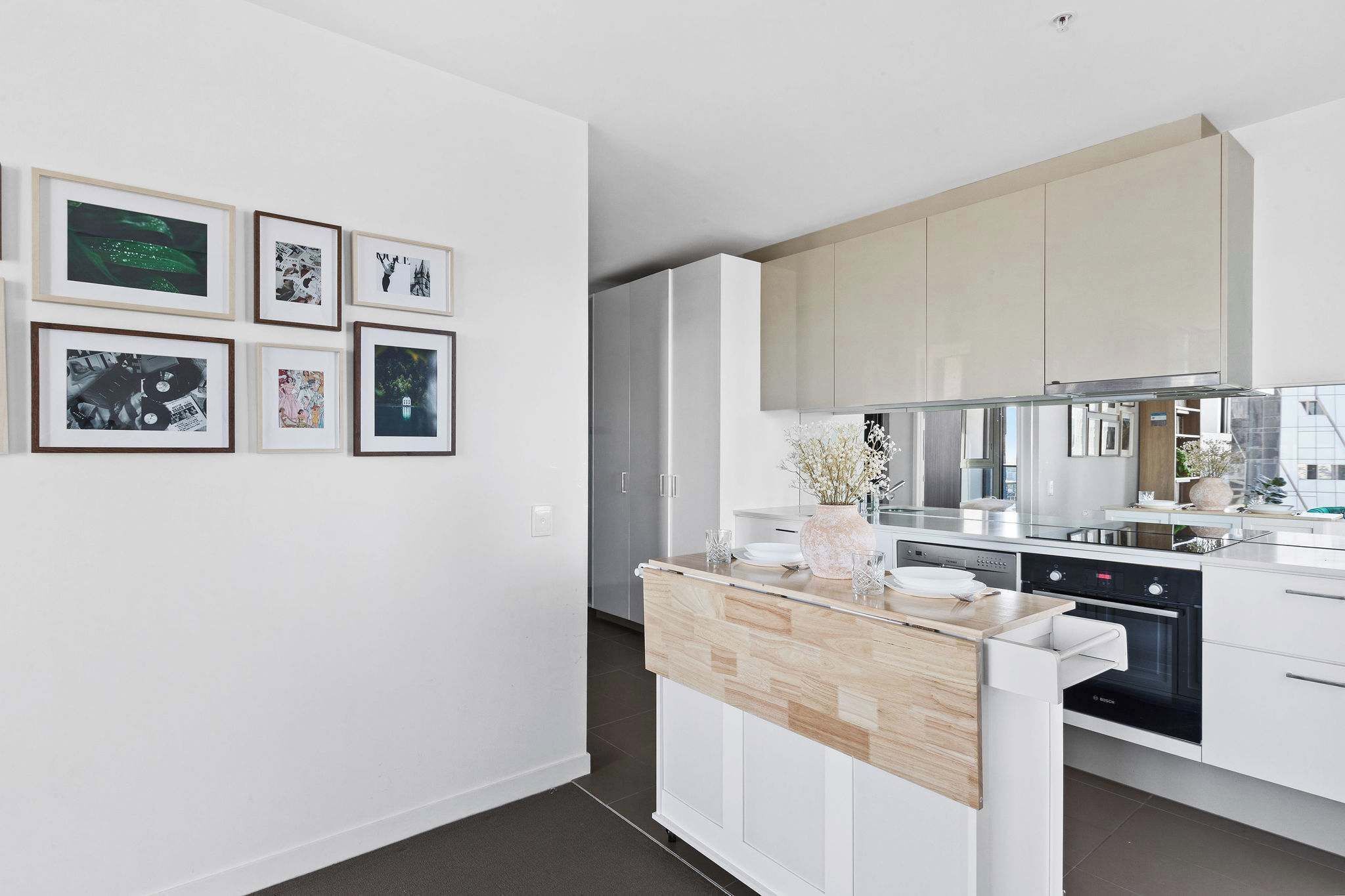 Een moderne keuken met witte kasten, een houten aanrecht en een Bosch oven. Er hangen fotolijstjes aan de muur en op het aanrecht staat een vaas met bloemen.