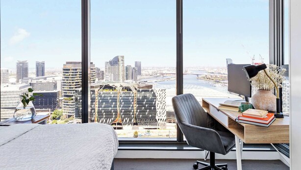 Habitación de hotel moderna con un amplio ventanal que ofrece vistas a la ciudad, un escritorio con computadora, libros y objetos decorativos.
