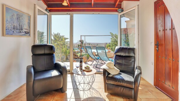Une pièce avec deux fauteuils en cuir, une petite table sur laquelle se trouvent une bouteille et des verres, et une grande porte vitrée donnant sur un espace piscine.