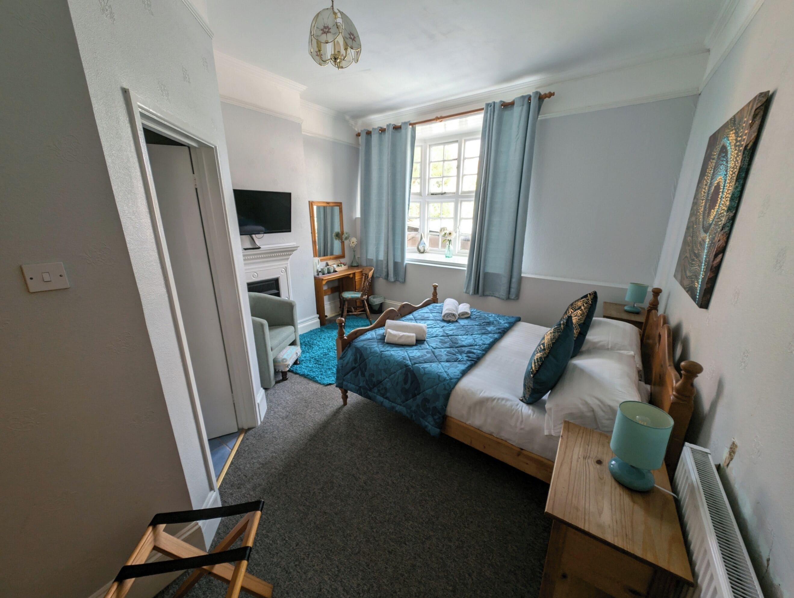 Un dormitorio con cama, escritorio, silla, televisión, ventana con cortinas y radiador.