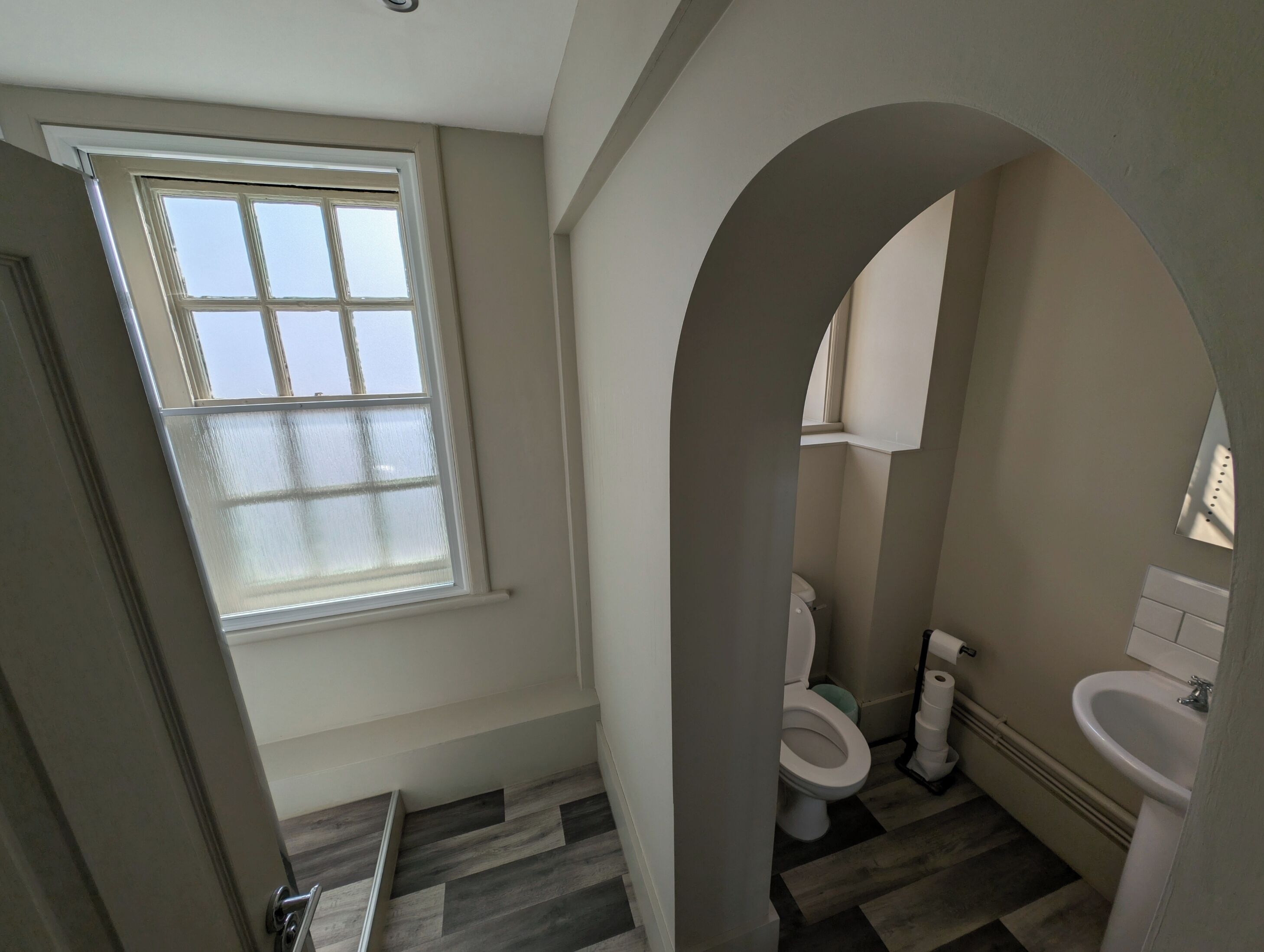 A bathroom with a window, a toilet, a sink, and a shower area.