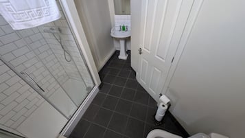 A bathroom with a shower, toilet, sink, and a towel hanging on the wall.