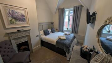 Une chambre à coucher avec un lit, une cheminée, une fenêtre avec des rideaux, un miroir et une table de chevet avec une lampe.