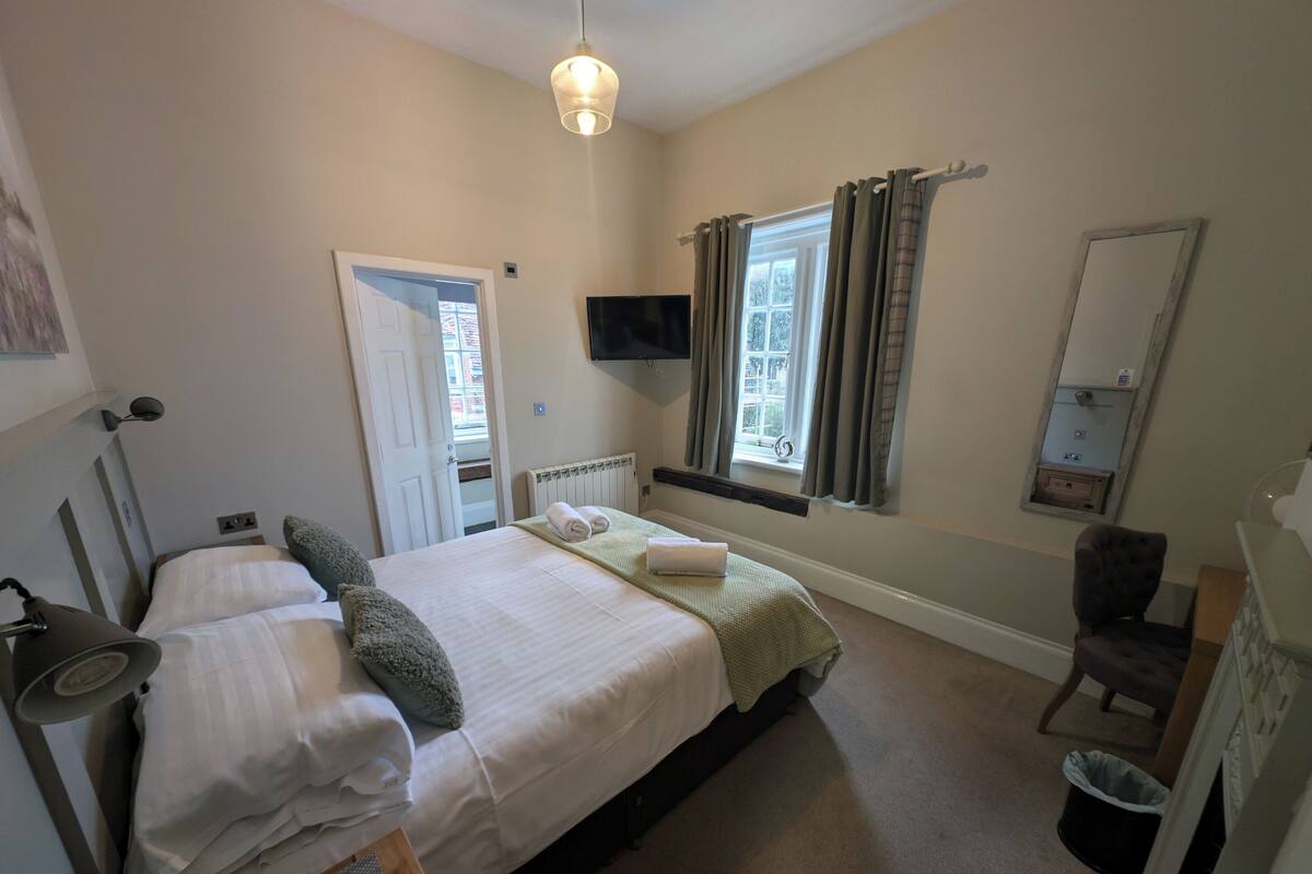 Un dormitorio con dos camas, televisión, ventana con cortinas, radiador y espejo.